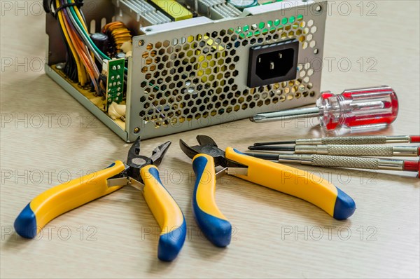 Side view of opened desktop power supply together with pliers and screwdrivers needed to repair