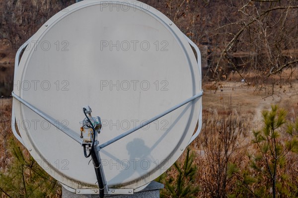 Closeup of satellite dish mounted on concrete column with riverside slightly blurred in background