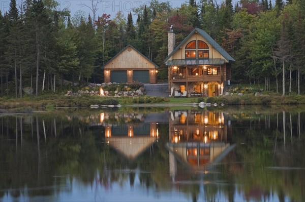 Illuminated two car garage and handcrafted two story spruce log cabin home with fieldstone chimney