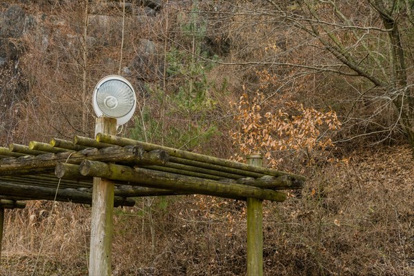 Halogen lamp in front of satellite TV dish on top of log structure in wooded mountainside park in