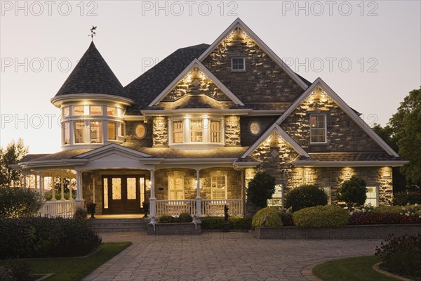 Elegant grey stone with white trim and blue asphalt shingles roof Victorian home facade at dusk in