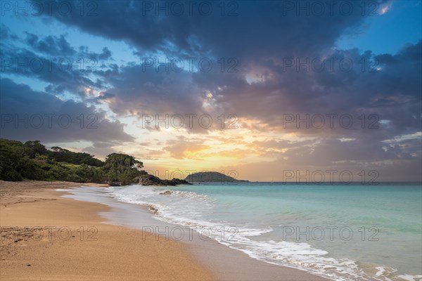 Lonely, wide sandy beach with turquoise-coloured sea. Tropical plants in a bay at sunset in the