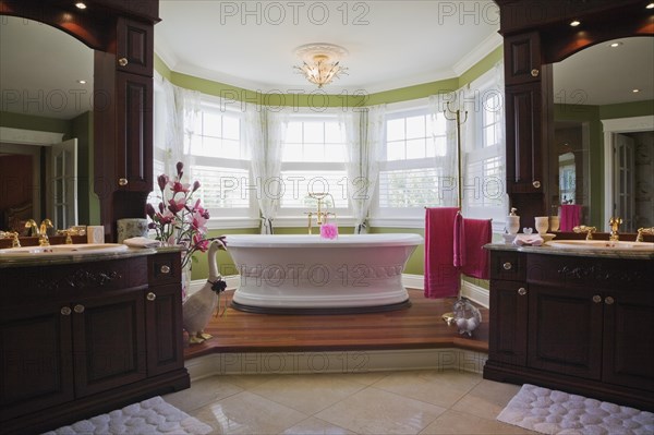 Master bedroom en suite with freestanding white bathtub on raised platform and his and her vanities