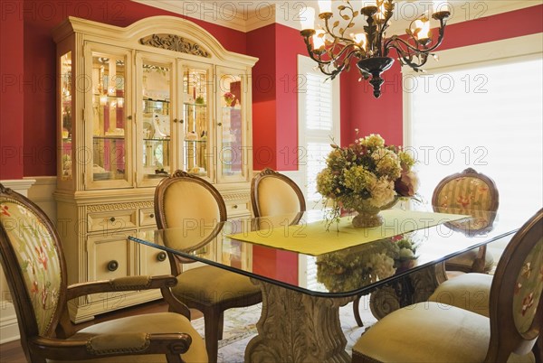 Glass top table with high-back wooden and upholstered chairs in dining room with buffet inside