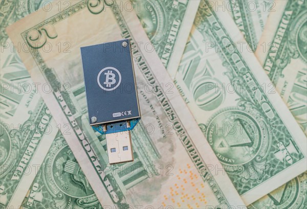 A dark blue USB hardware wallet with a Bitcoin logo on a background of US dollar bills, in South