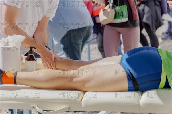 An athletic trainer wearing a white t-shirt is providing a professional leg massage to a runner