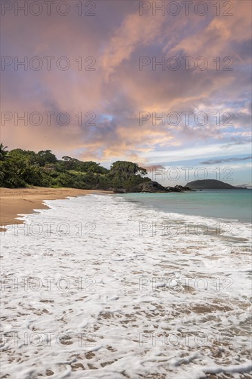 Lonely, wide sandy beach with turquoise-coloured sea. Tropical plants in a bay at sunset in the