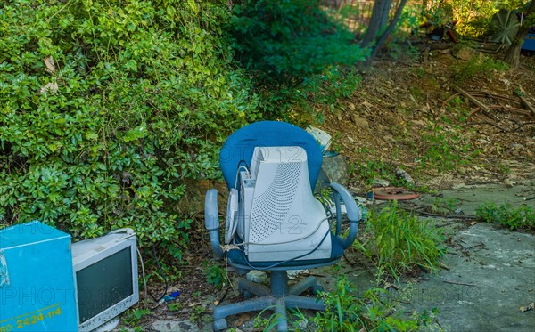 Old CRT computer monitors discarded in rural wooded area. One in old chair the other on the ground