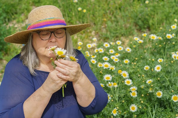Mature woman with white hair and hat with a bouquet of daisies in her hands, in the background a