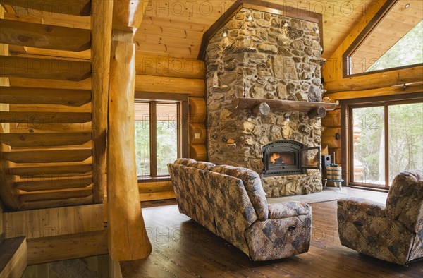 Wooden log stairs and upholstered sofas with lit fieldstone and porous rock fireplace in living