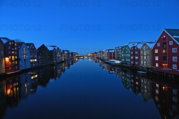 Historic warehouse buildings reflected in the river Nidelva at dusk, Bryggene, Trondheim, Norway,