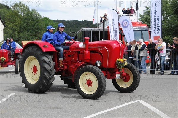 Porsche Diesel Tractors, A red vintage tractor is presented at an event, driver in blue overall,
