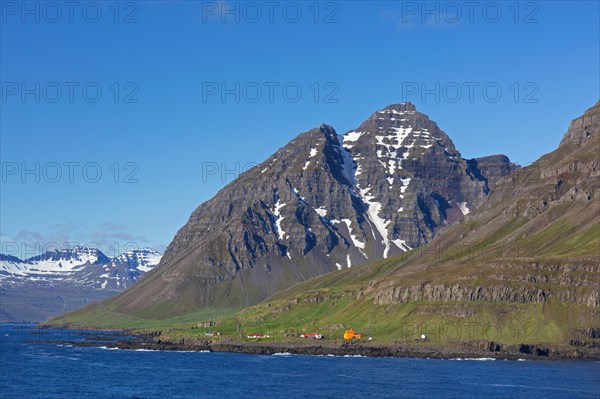 Rugged mountains and orange lighthouse at Skalanes along the fjord Seyoisfjoerour, Seydisfjoerdur