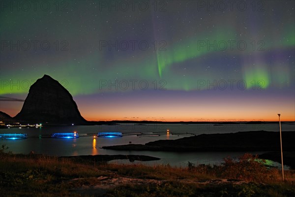 Northern lights (aurora borealis) mingle with sunset, sea, striking mountains and fish farm,