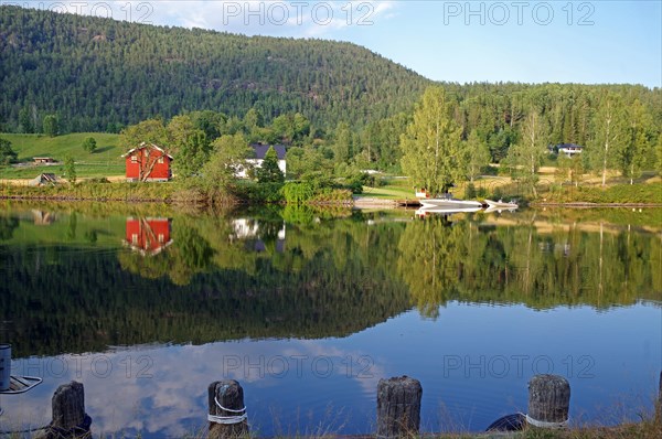 Trees, houses and a small boat are reflected in a calm lake, old waterway, Telemark Canal,