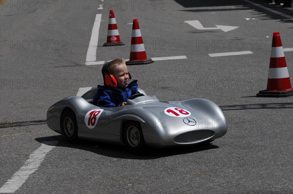 Smiling child enjoying a ride in a silver soapbox on a closed-off road, SOLITUDE REVIVAL 2011,