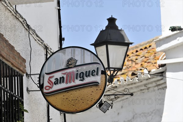 Solabrena, A round beer advertising sign for San Miguel on a wall next to a lantern, Andalusia,
