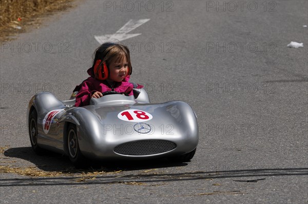 A small child concentrates while driving a silver soapbox with the number 18, SOLITUDE REVIVAL