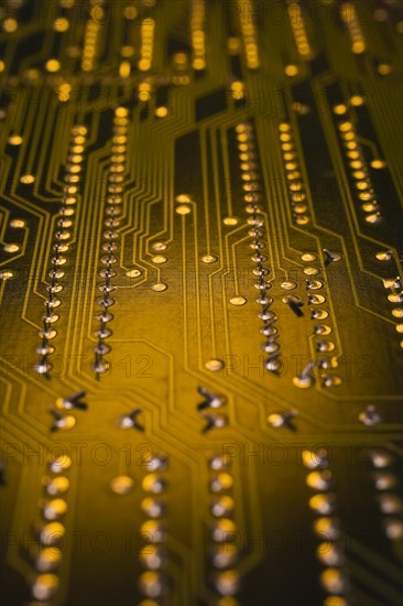 Close-up of golden yellow lighted electronic computer circuit board with lines and silver solder