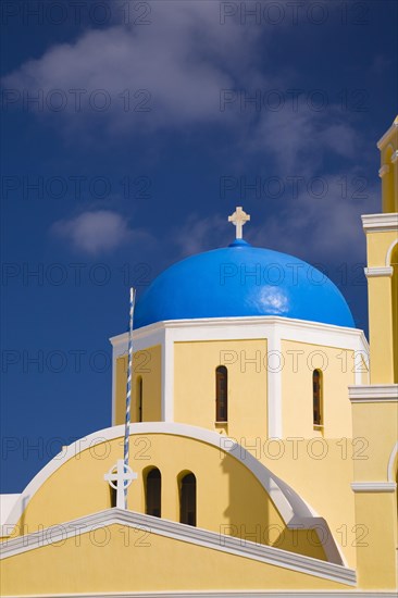 Close-up of yellow painted roughcast cladded chapel with cross on blue dome, Oia village,
