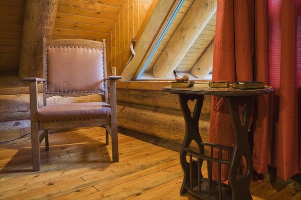 Brown wooden leather armchair and side table in master bedroom with red curtains and wood plank