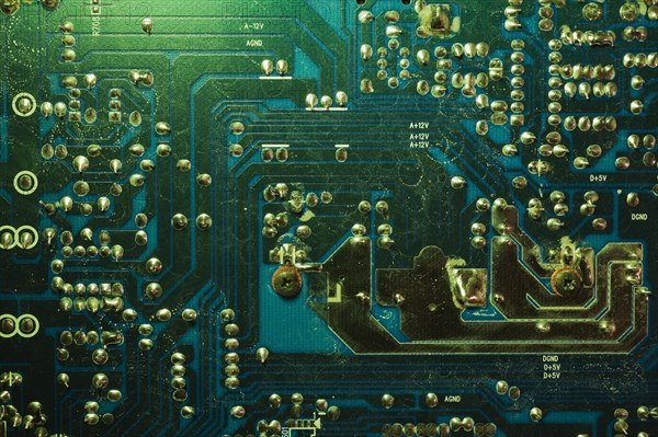 Close-up of green lighted electronic computer circuit board with silver solder points and lines,