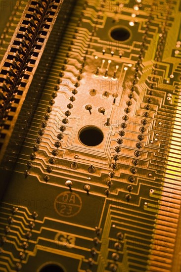 Close-up of golden orange and yellow lighted electronic computer circuit board with silver solder