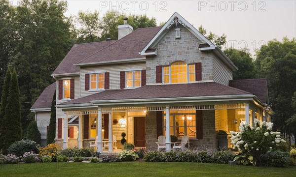 Large illuminated two story beige and tan cut stone home exterior with white and red trim, multiple