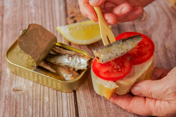 A woman puts a sardine on a slice of bread with tomato, in the background you can see the can of