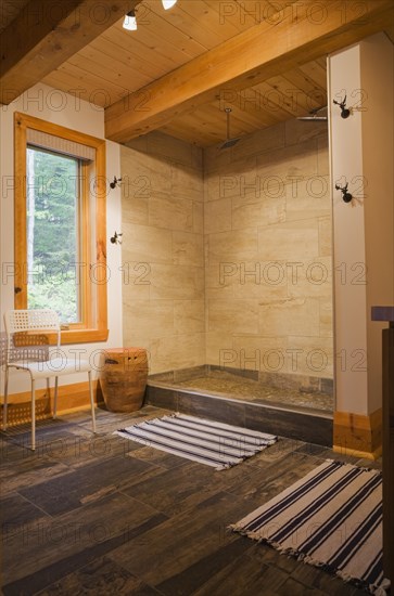 Illuminated beige ceramic shower stall in main bathroom with tan and dark grey ceramic tile floor