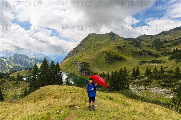Woman 60-65 hiking with umbrella, behind her Seealpsee and Seekoepfel, 1919m, Allgaeu Alps,