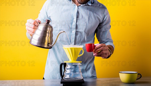 Man with kettle pouring water into a pour-over coffee maker against a vibrant yellow background,