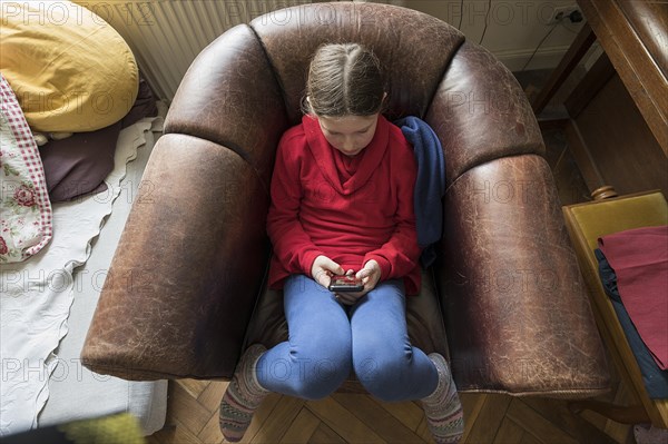 Symbol photo mobile phone, internet, addiction, little girl, 10 years old, sitting in an armchair