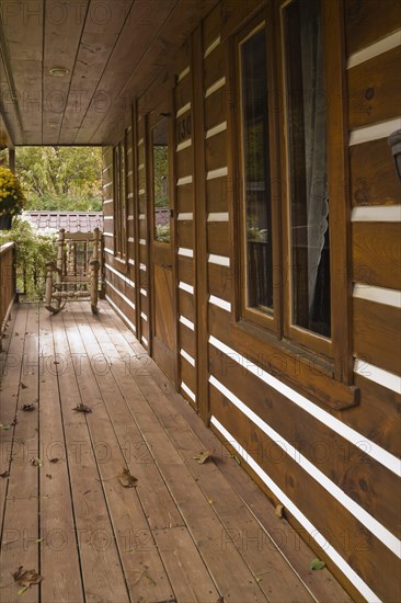 Long old and worn brown stained veranda with pine wood rocking chair on facade of rustic white