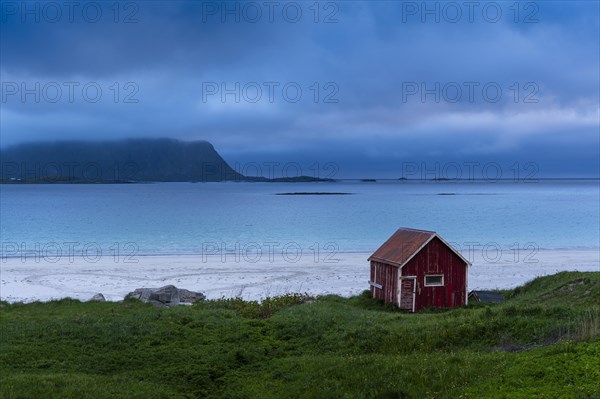 A red wooden hut on the sandy beach of Ramberg (Rambergstranda), sea and mountains. At night at the