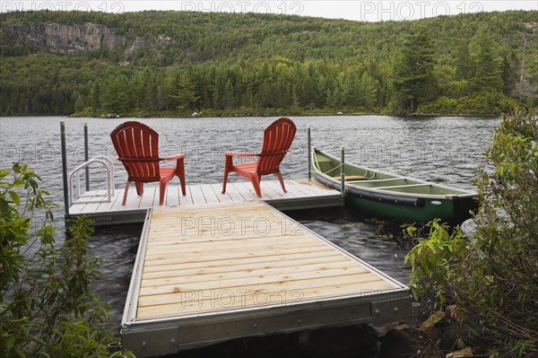Two bright red plastic Adirondack chairs on floating wooden dock and green rowboat on calm lake