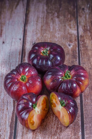 Group of tasty fresh tomatoes of the blue variety with a halved tomato dipped in water drops on a