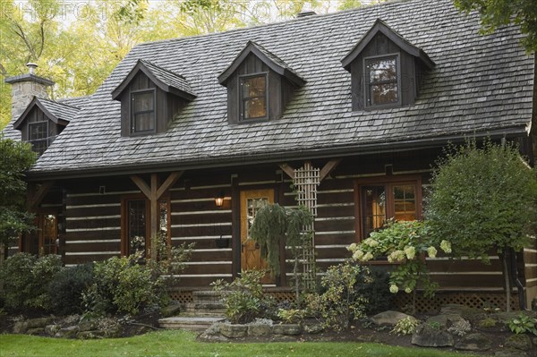 White chinked log cabin home facade with grey weathered cedar shingles roof, three dormer windows