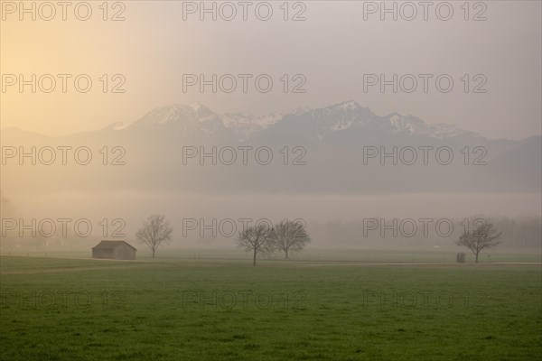 A landscape in the morning mist with a small hut and mountains in the background, Neubeuern,