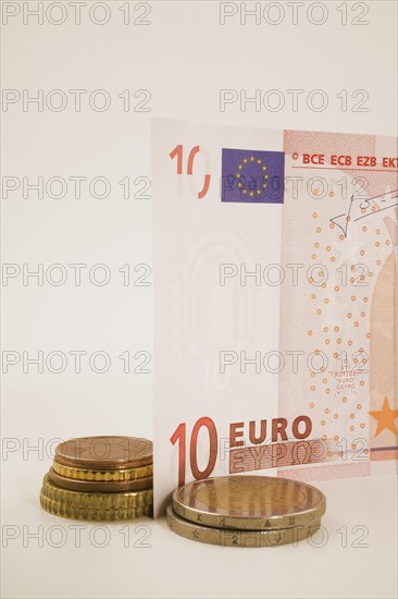 Close-up of 10 Euro bank note and piles of assorted gold and copper colored coins on white