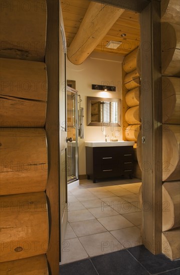 Wooden vanity with white rectangular sink in illuminated guest bathroom with tan ceramic tile floor