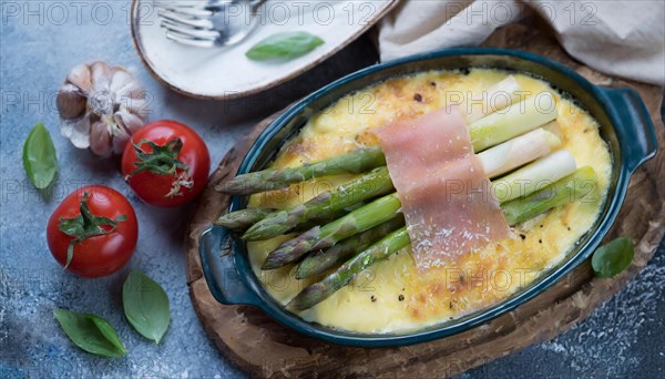 Fine asparagus gratin garnished with fresh cherry tomatoes and garlic on a wooden base, asparagus