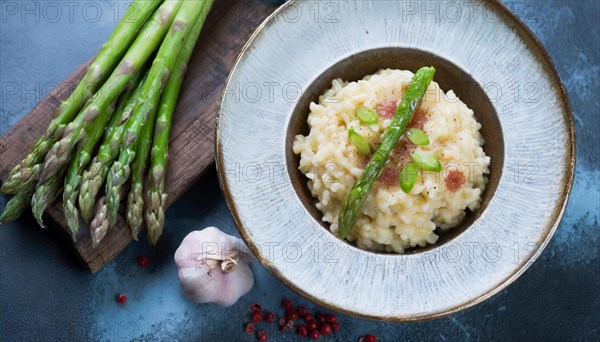 A plate of risotto with asparagus and pieces of bacon next to garlic cloves, risotto with green