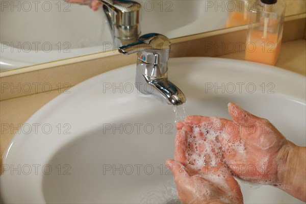 A woman washes her hands under the faucet. A stream of drinking water flows into the bathroom sink.