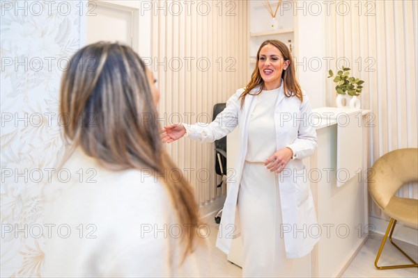 Female aesthetic doctor with lab coat and elegant clothes welcomes a patient at the entrance of a