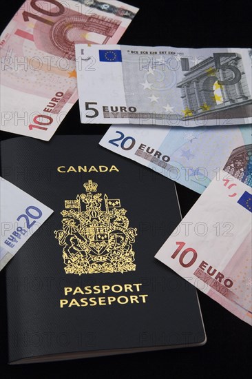 Close-up of five, ten, twenty Euro paper currency bank notes on top of Canadian passport on black