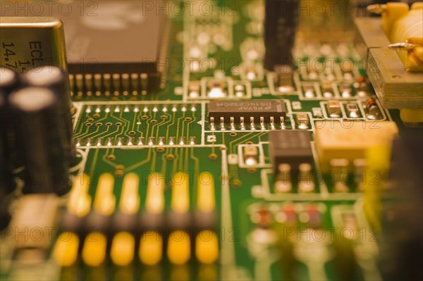 Close-up of green and golden lighted yellow electronic computer circuit board with capacitors,
