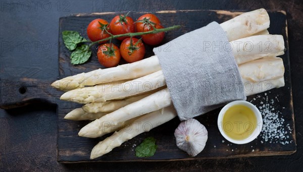 Bunch of white asparagus on a wooden board with tomatoes, garlic and oil, bunch of white asparagus