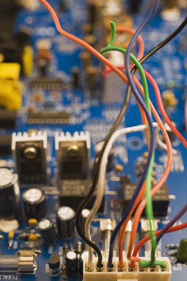 Close-up of colorful insulated electrical wires and blue computer circuit board with capacitors and