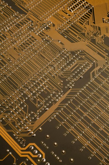 Close-up of golden orange lighted electronic computer circuit board with lines and silver solder